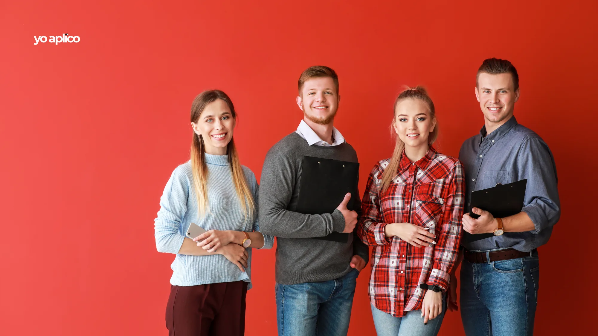 Cuatro personas jóvenes de pie, una al lado de otra. Dos llevan una carpeta y una, el celular.